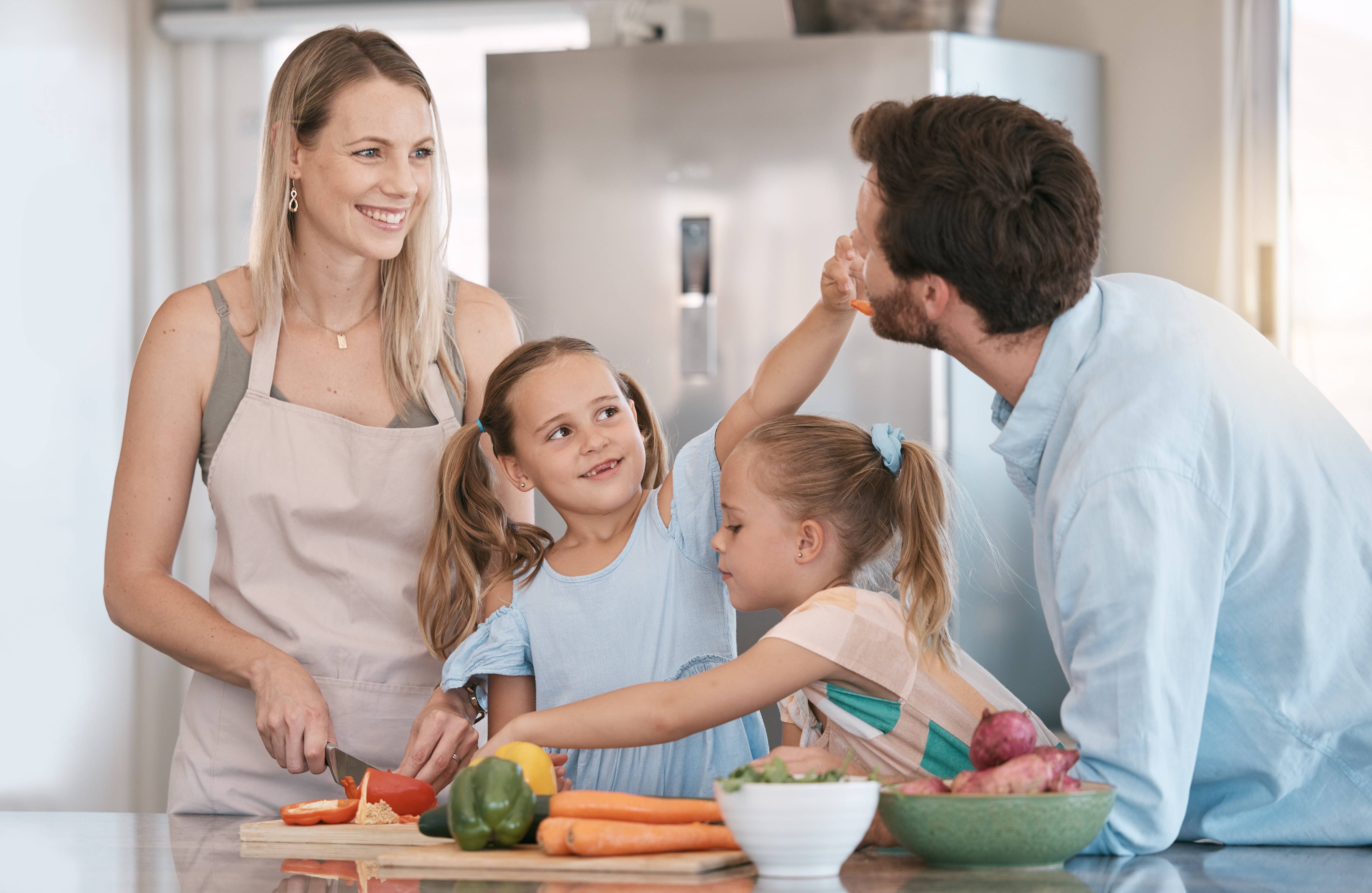A family cooking together in a bright kitchen with a large refrigerator in the background — the everyday scene appliance repair keeps running.
